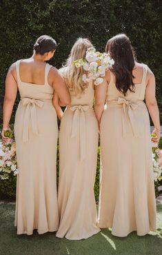 three bridesmaids are standing in front of some bushes and looking at each other