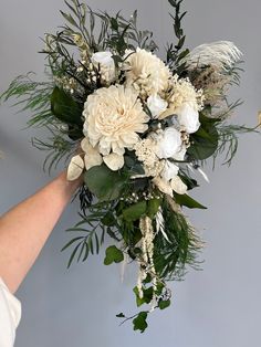 a bouquet of white flowers and greenery being held by a woman's hand