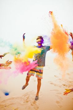 a group of people throwing colored powder on each other in the air at the beach