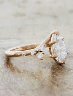 an engagement ring with two pear shaped diamonds on it, sitting on top of a wooden table