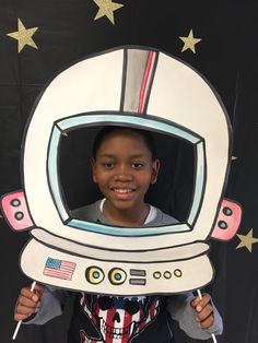 a young boy holding up a cardboard cutout of an astronaut's helmet with the american flag on it