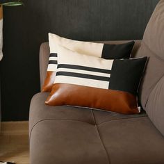 two pillows sitting on top of a brown couch next to a vase with flowers in it