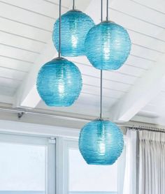 three blue lanterns hanging from the ceiling in a living room with white walls and windows