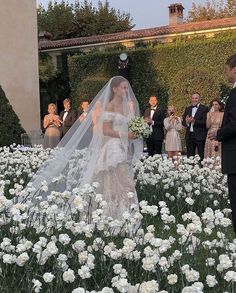 the bride and groom are standing in front of their wedding party, surrounded by white flowers