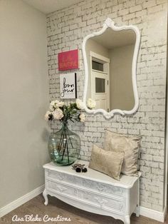 a white bench sitting in front of a mirror on the wall next to a vase with flowers