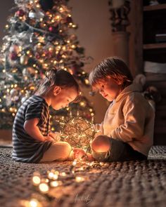 two young children sitting on the floor next to a christmas tree and looking at a lit candle