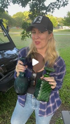 a woman standing in front of a car holding two green vases and a bottle