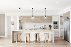 an open kitchen with three stools in front of the island and two lights hanging from the ceiling