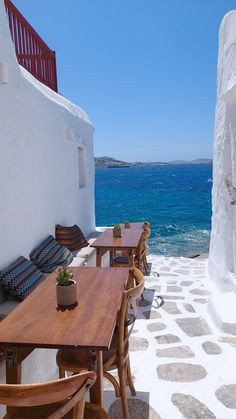 an outdoor dining area overlooking the ocean with wooden tables and chairs on it's side