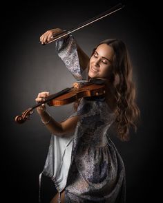 a woman is playing the violin and posing for a photo in front of a black background