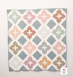 a quilt is hanging on the wall in front of a white wall with an orange and blue checkered design