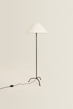 a floor lamp with a white shade on the top and a black cord attached to it