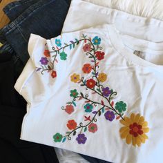 three t - shirts with embroidered flowers on them, one white and one black are sitting next to each other