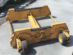 a toy car made out of wood sitting on top of a cement surface next to a parking lot