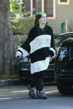 a woman with green hair is walking down the street wearing a black and white sweater