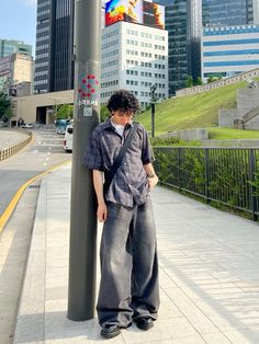 a man standing next to a pole on the side of a road with tall buildings in the background