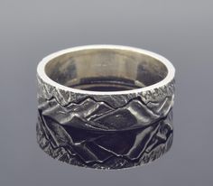 a silver ring with an intricate design on the outside and inside, sitting on a gray surface