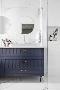 a bathroom with marble counter tops and blue cabinetry on the vanity, along with two round mirrors