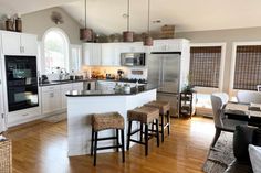 a large kitchen with white cabinets and wooden floors is pictured in this image, there are stools at the center of the island