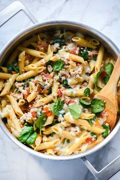 a pot filled with pasta and spinach on top of a marble countertop next to a wooden spoon