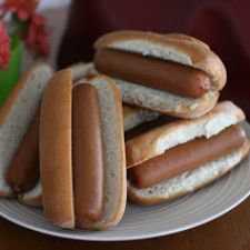 several hotdogs are on a plate with buns and flowers in the background