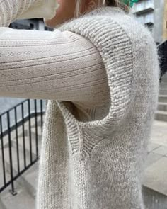 a woman is standing on the sidewalk with her cell phone to her ear and wearing a white sweater