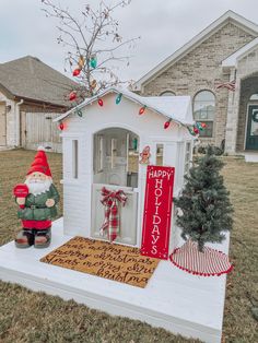 a small white house decorated for christmas with a santa clause decoration on the front door