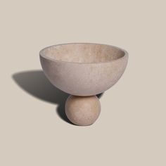 a large white bowl sitting on top of a stone ball in front of a gray wall