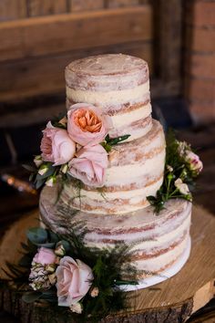 a three tiered cake with flowers and greenery sits on top of a tree stump