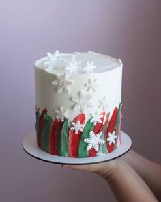 a hand holding a white frosted cake with snowflakes on it