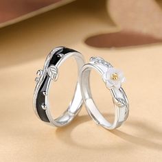 two wedding rings with black and white enamel flowers on each ring, set against a beige background