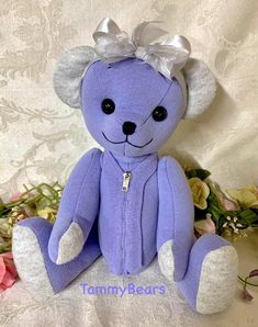 a purple teddy bear with a white bow sitting on a table next to some flowers