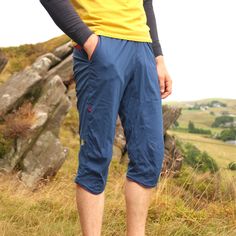 a man standing on top of a grass covered hillside next to a rock formation with his hands in his pockets