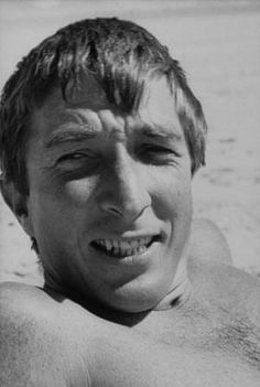 a black and white photo of a shirtless man on the beach with his eyes closed