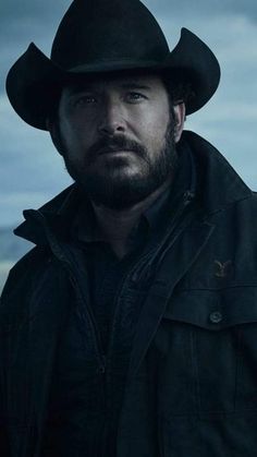 a man with a beard wearing a black cowboy hat and jacket looking at the camera