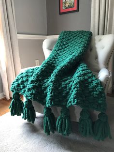 a green crocheted blanket sitting on top of a white chair next to a window