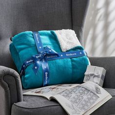 a gray chair with a blue blanket on top of it and a magazine laying next to it