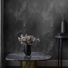 a vase with flowers on a marble table in front of a black and white wall