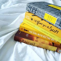 a stack of books sitting on top of a white sheet covered bed next to each other