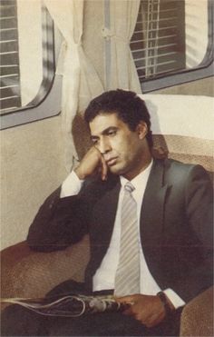 a man in a suit and tie sitting on a train with his hand to his face