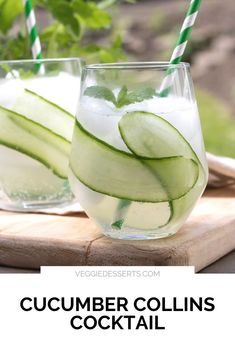 two glasses filled with cucumber drinks on top of a cutting board