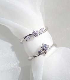 two diamond rings sitting on top of a white cloth next to a piece of fabric