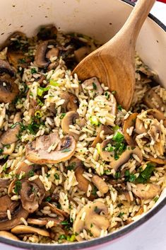 a pot filled with rice and mushrooms on top of a table next to a wooden spoon