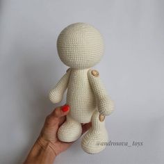 a hand holding a small white knitted teddy bear in front of a white background