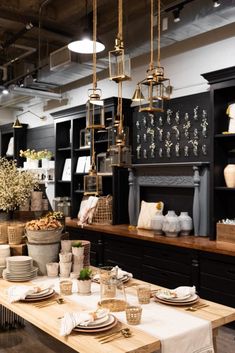 a table with plates and cups on it in a room filled with black cabinets, hanging lights, and chandeliers