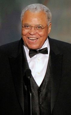 an older man in a tuxedo smiles as he stands at a podium with a microphone