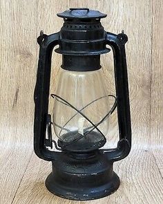 an old fashioned black lantern on a wooden table with a light bulb in the middle