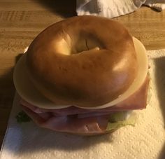 a bagel sandwich with ham and lettuce on it sitting on a napkin