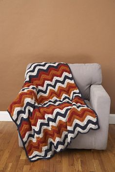 an orange and blue blanket sitting on top of a couch next to a white chair