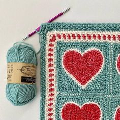 a crocheted square with hearts on it next to a ball of knitting yarn